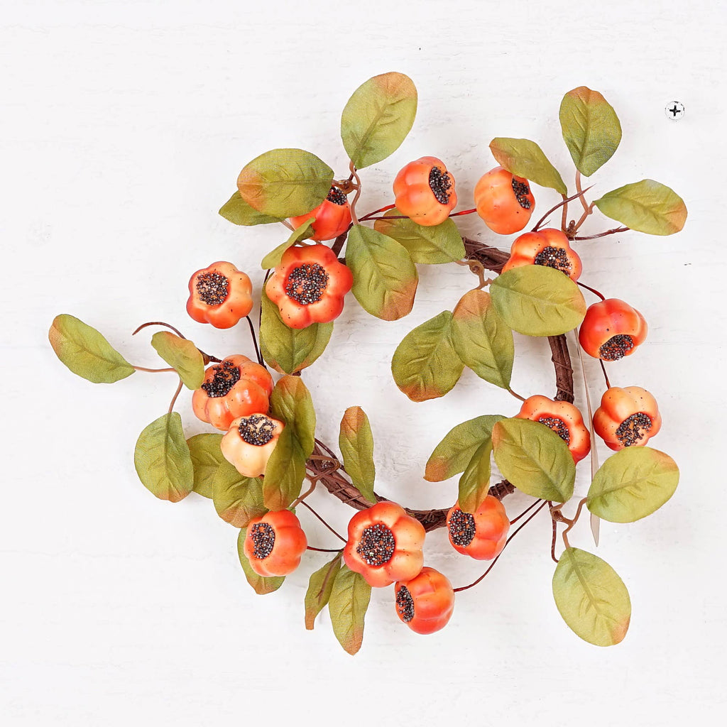 An artificial autumn wreath featuring orange berries with dark centers and green leaves on a white background.