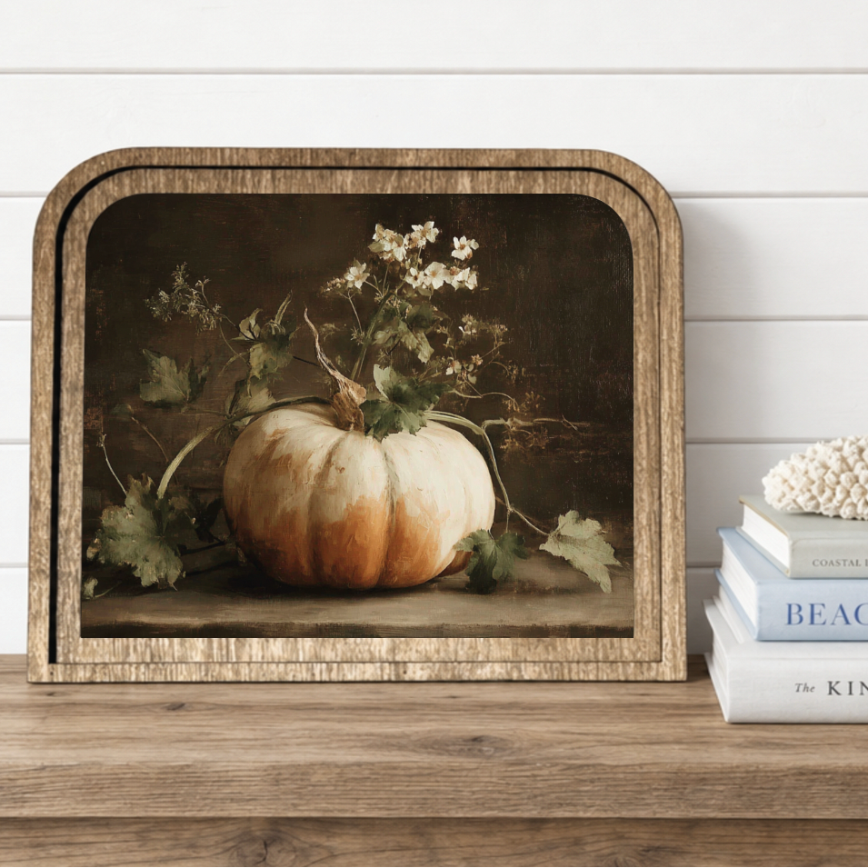 Framed artwork of a pumpkin and flowers on a wooden shelf with books below.