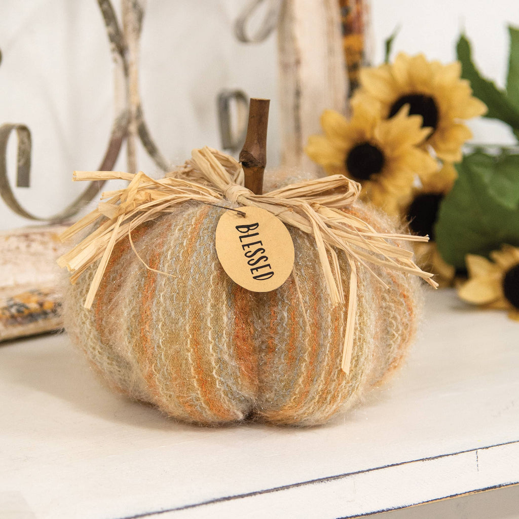Decorative pumpkin with a 'blessed' tag on a white surface with sunflowers in the background