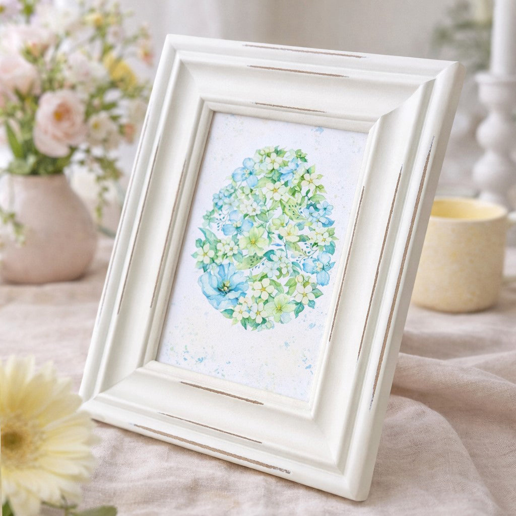 Framed floral Easter egg art print featuring delicate blue, green, and cream blossoms in egg-shaped design, displayed in distressed white 6.5x8.5 inch frame for spring decor