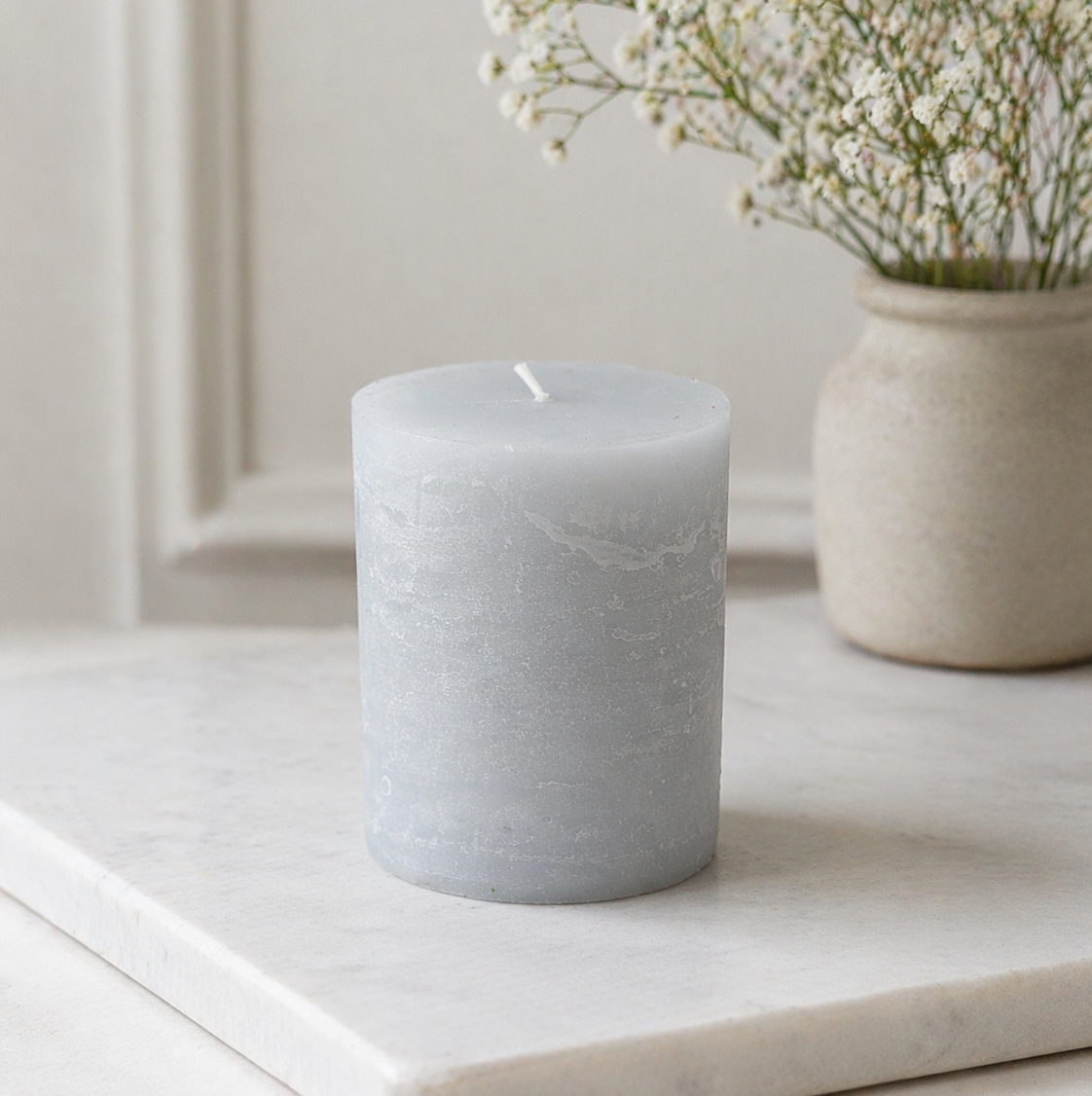 Gray candle on a white surface with a vase of flowers in the background