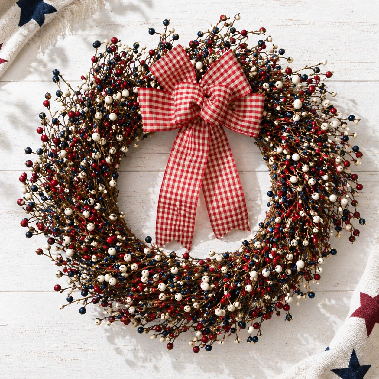 Red, white, and blue berry wreath with red, white, and blue berries and a checkered bow on a white background