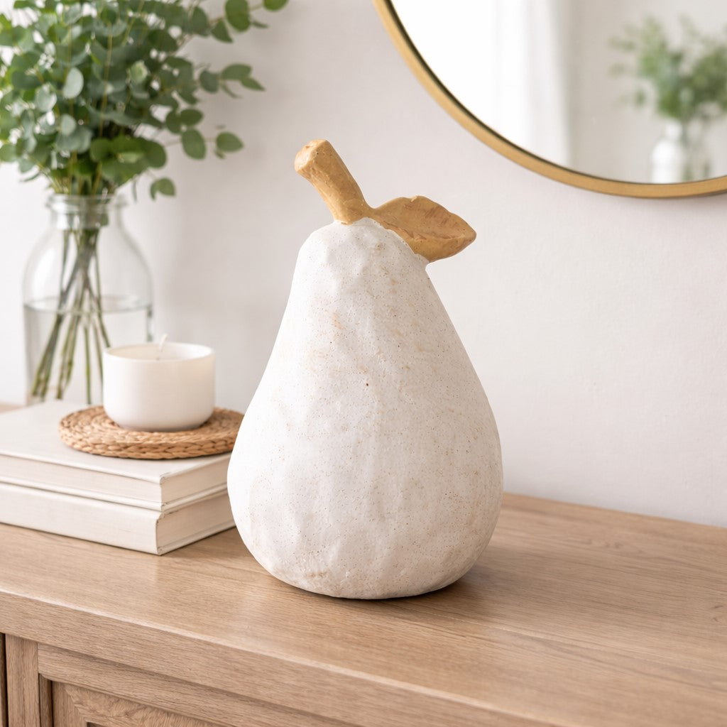 Decorative pear-shaped object on a wooden surface with a candle and books in the background.