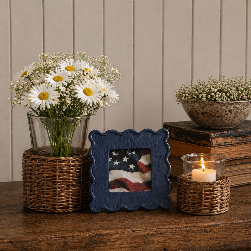 Decorative setup with flowers, picture frame with patriotic flag, candle, and books on a wooden surface.