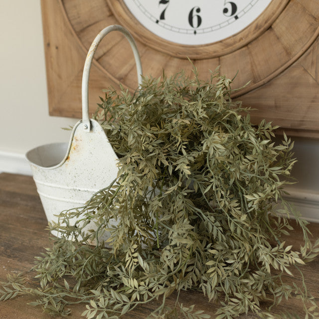 Faux greenery with a white bucket and wooden clock in the background