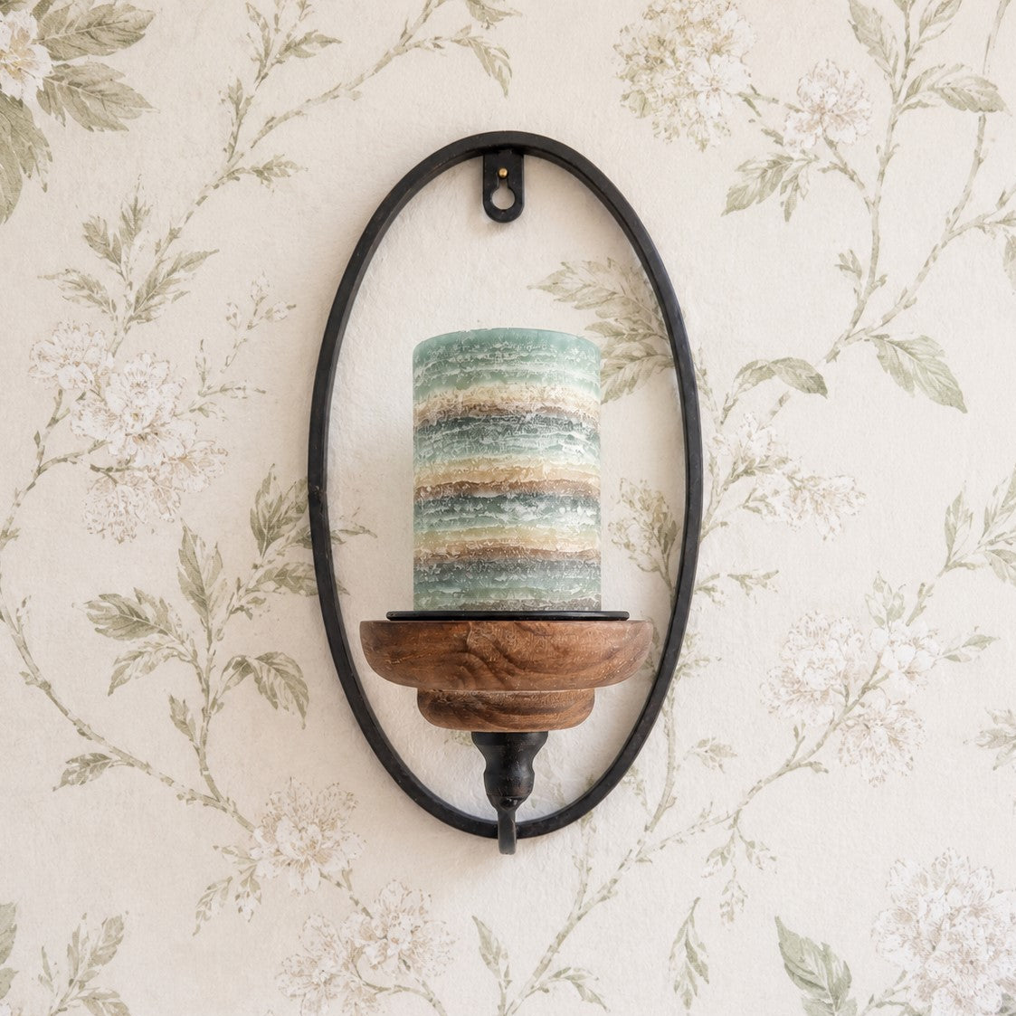 Wall-mounted candle holder with a striped candle against a floral wallpaper background