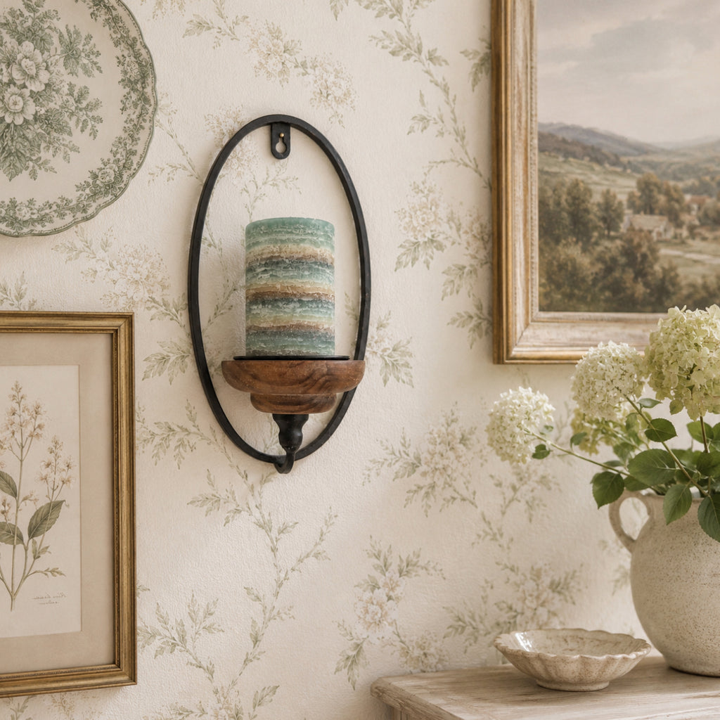 Decorative wall sconce with a candle, framed artwork, and a vase of flowers on a floral wallpapered wall.