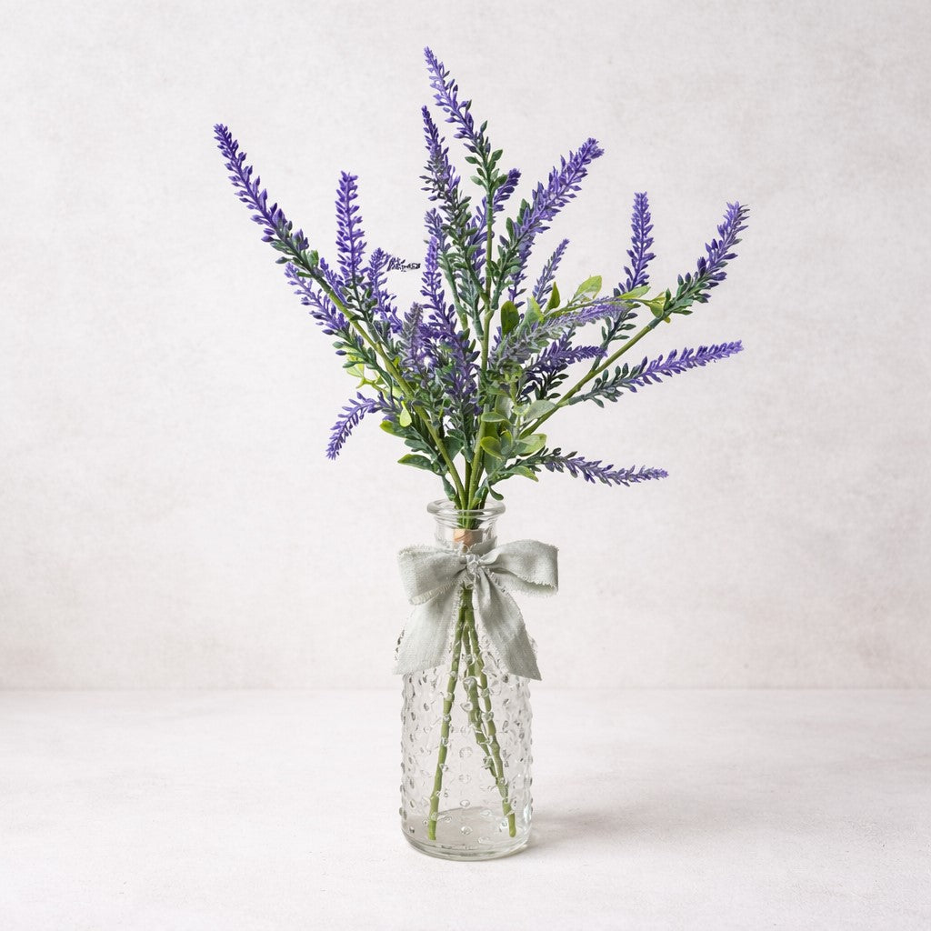 Clear glass vase with lavender flowers and a silver bow on a light gray background