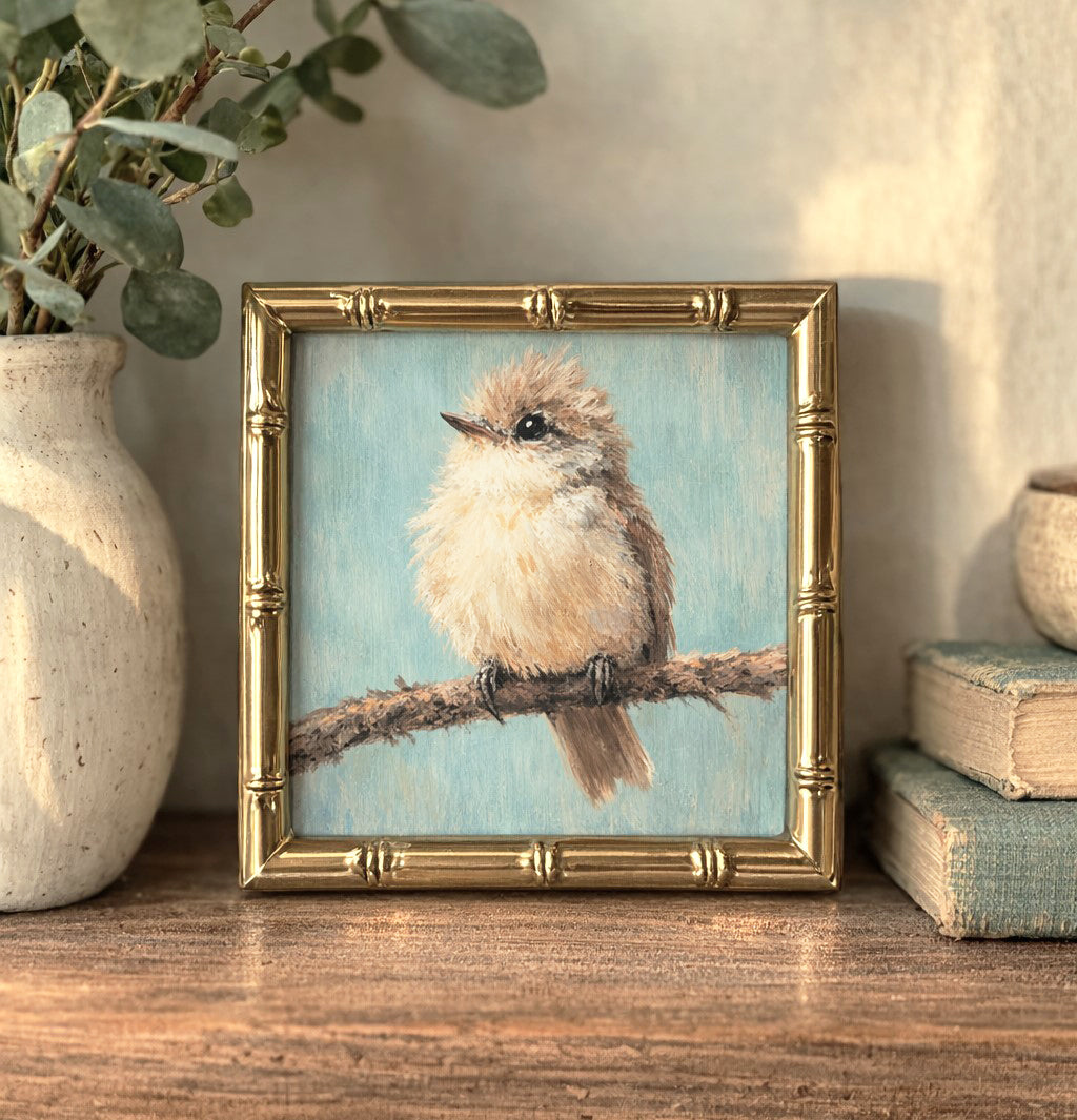 Framed artwork of a bird on a branch with decorative elements on a wooden surface.