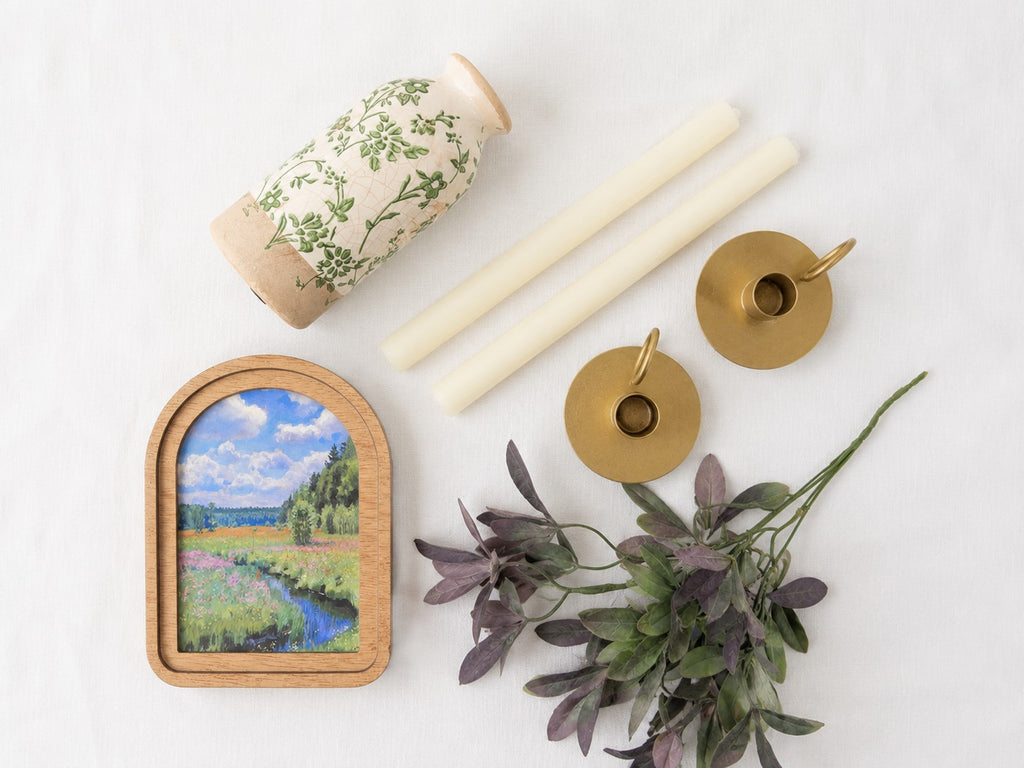 Decorative items including a small framed painting, candles, and plants on a white surface