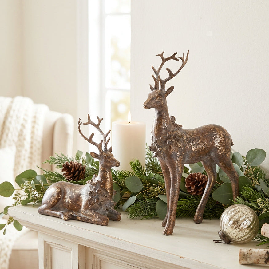Two decorative deer figurines with a distressed bronze finish, one standing and one lying down, photographed on a seamless white background.