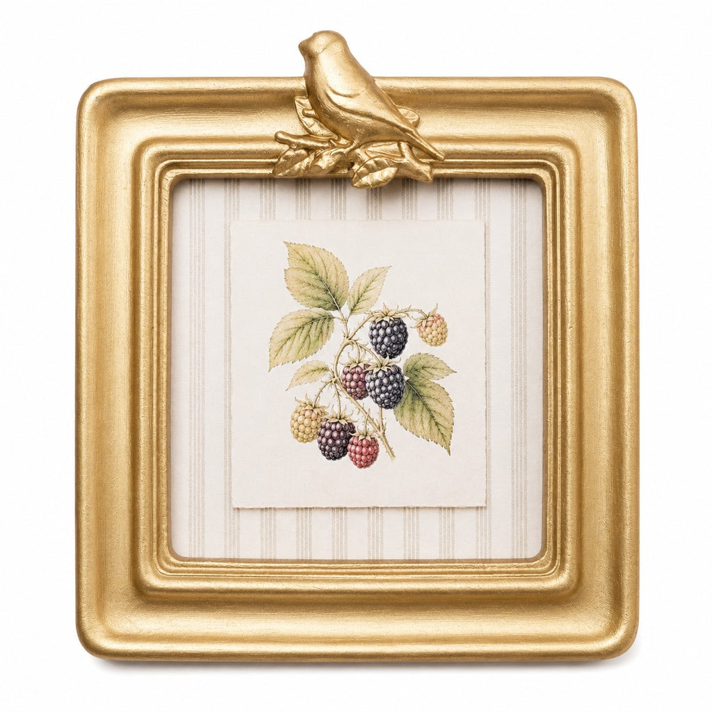 A square gold picture frame with a decorative bird perched on the top edge, holding a small botanical print of blackberries on a cream striped background.