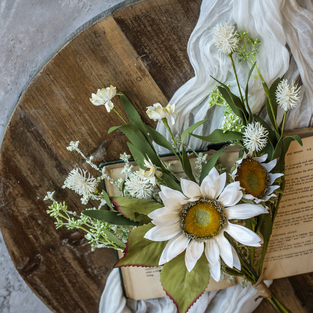 Floral arrangement with creamy sunflowers flowers and green leaves on a wooden surface.
