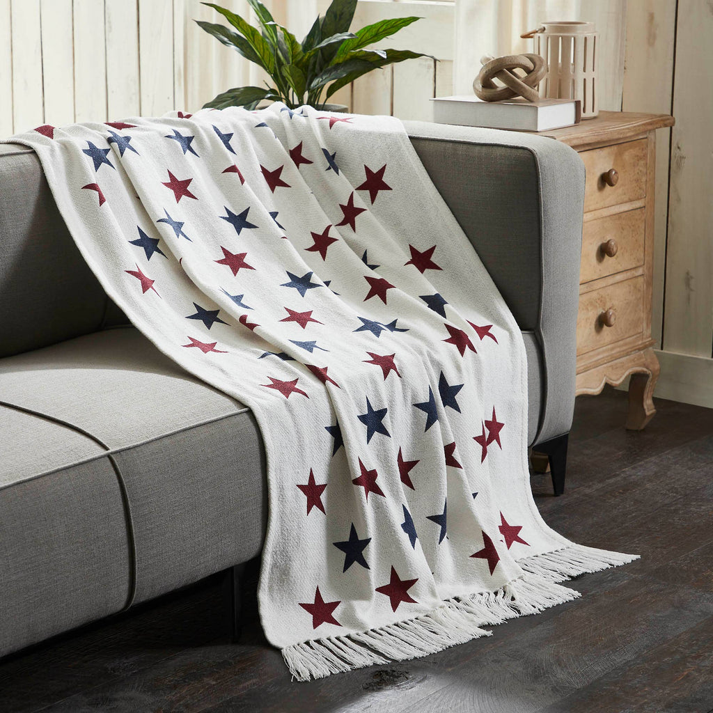 White blanket with red and blue star pattern draped over a gray sofa in a living room setting.