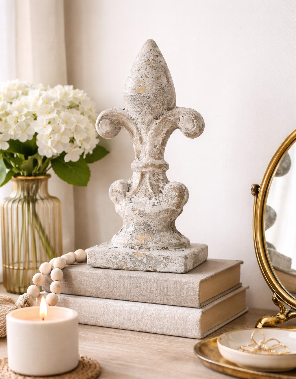 Decorative stone fleur-de-lis sculpture on books with a candle and flowers in the background