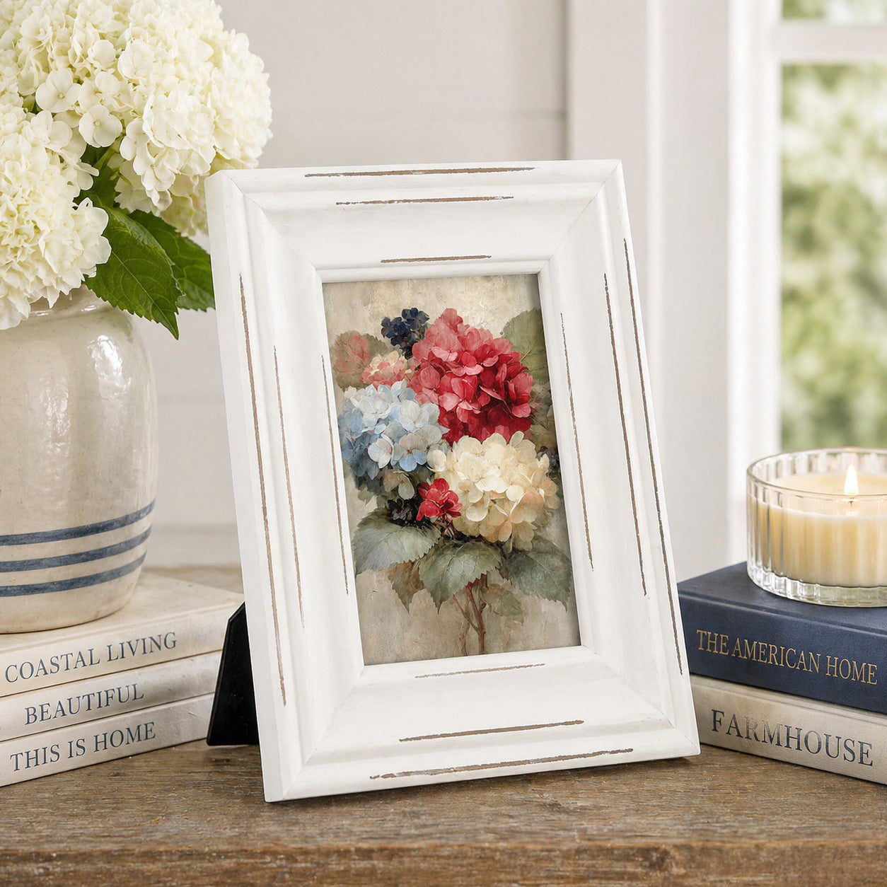 White framed floral print on a wooden surface with books and a candle in the background